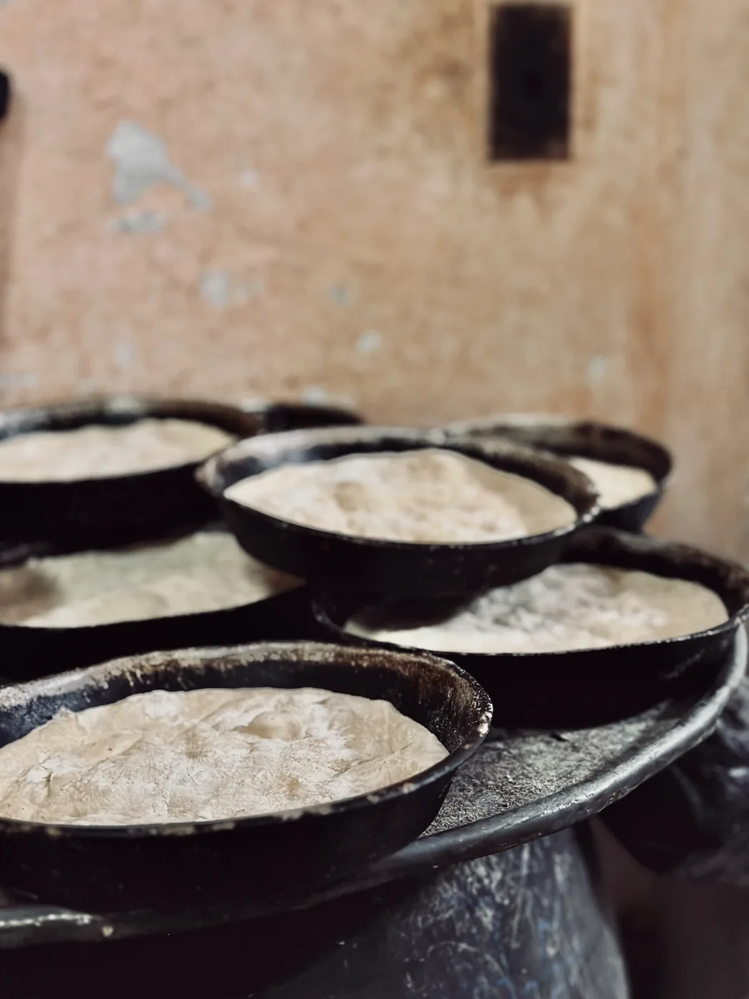 Iron pans with dough proving, stacked against the wall