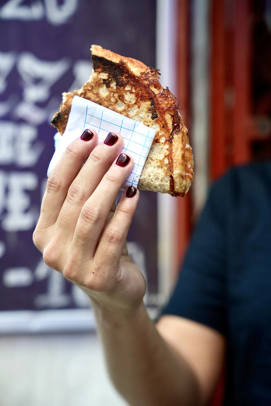 A slice of pizza on a scrap of paper, held in one hand out in the street